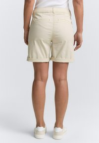 Shorts beige avec ourlet roulé en coton, dotés de deux poches arrière et d'une texture lisse, associés à des baskets blanches.