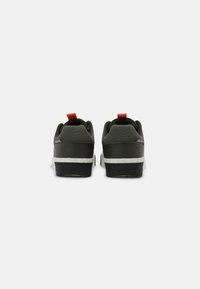 Green sneakers with a textured upper, white midsole, and black outsole. Features a red pull tab and prominent heel contour.