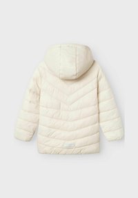 Chaqueta acolchada color crema con capucha, mangas largas y costuras en forma de chevron en la parte trasera, mostrada sobre un fondo liso.
