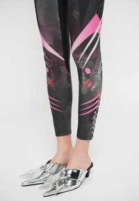 Tights med svart base, med rosa og hvite grafiske detaljer, og et skinnende mønster. Kombinert med sølvfargede mules med spiss tå.