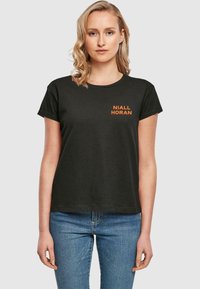Sort bomulds-t-shirt med rund halsudskæring og korte ærmer, med orange tekst "NIALL HORAN" på venstre brystområde.
