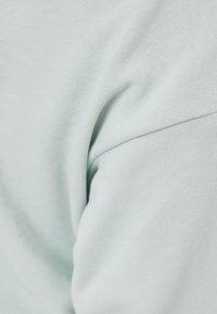 Světle zelená bavlněná látka s jemnou texturou a hladkým povrchem, se zdůrazněným švem a zakřiveným tvarem.