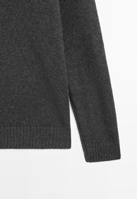 Tmavě šedý svetr s žebrovanou strukturou, kulatým výstřihem a dlouhými rukávy. Lem a manžety jsou rovněž žebrované pro zvýraznění detailů.