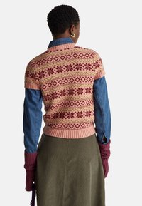 Pletený svetřík s krátkými rukávy s růžovými, červenými a zelenými květinovými a geometrickými vzory, kombinovaný s džínovou košilí a olivovou sukní.