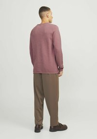 Lange mouwen bordeaux shirt met een ronde halslijn, gecombineerd met losse bruine broeken en zwarte leren schoenen, gezien vanaf de achterkant.