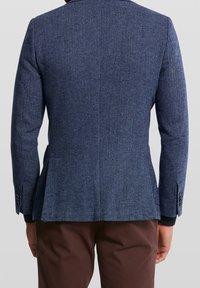 Marinblå herringbone-blazer med skräddarsydd passform, enkel slits och knappdetaljer vid ärmarna. Tillverkad av texturerat tyg, som visar på experthantverk.