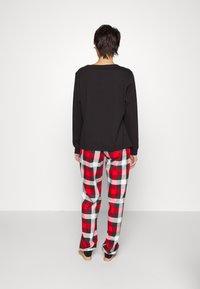 Haut noir à manches longues associé à un pantalon de pyjama à carreaux rouges et noirs. Le tissu semble doux, avec une coupe décontractée et un design simple.