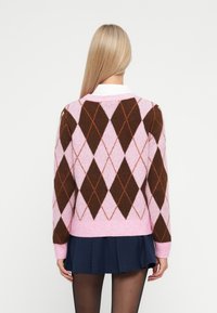 Rožinė ir ruda argyle rašto megztinis su ilgomis rankovėmis, minkšta tekstūra, raukšlėtos rankogaliai ir apdaila, derinama su tamsiai mėlyna klostuota sijonė.