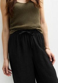 Olijfgroene gebreide tanktop met een ronde hals, gecombineerd met losse zwarte broek met een trekkoord in de taille en een gekreukt textuur.