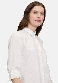 Weißes Hemd aus leichtem Stoff, mit klassischem Kragen, hochgekrempelten Ärmeln und Knopfdetails entlang der Vorderseite.