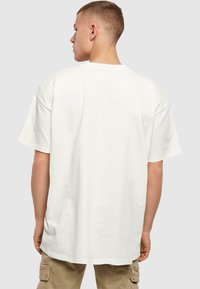 Witte katoenen t-shirt met een ontspannen pasvorm, verlaagde schouders en een ronde halslijn. De stof lijkt glad met een minimalistisch ontwerp.