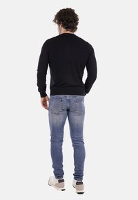 Suéter negro de punto, diseño ajustado, puños y dobladillo acanalados, combinado con jeans ajustados de color azul claro. Costuras y detalles de bolsillo visibles.
