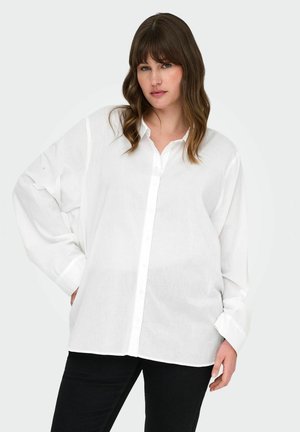 Camicia bianca con bottoni realizzata in tessuto leggero, con maniche lunghe e vestibilità rilassata. Abbinata a pantaloni neri.