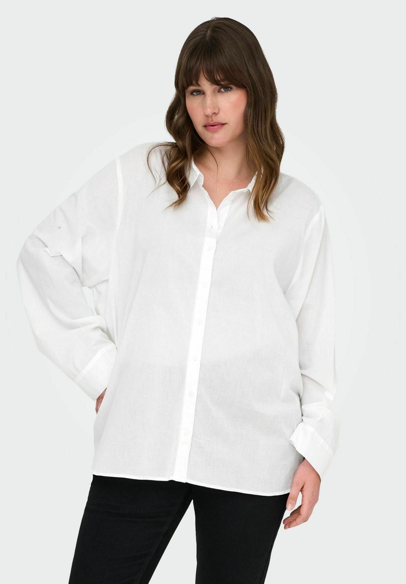 Camicia bianca con bottoni realizzata in tessuto leggero, con maniche lunghe e vestibilità rilassata. Abbinata a pantaloni neri.