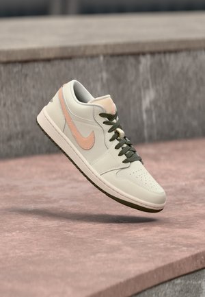 Scarpa da ginnastica bianca e pesca con lacci neri che fluttua sopra una superficie in cemento rosa e grigia.