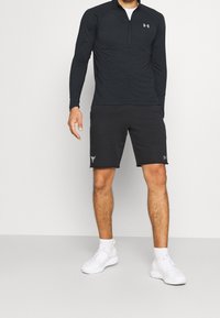 Černý dlouhý rukáv s čtvrtzipem a přiléhavým střihem v kombinaci s černými šortkami. Outfit doplňují bílé sportovní boty.