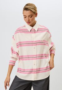 Hvid skjorte med lyserøde og grå vandret striber. Har en klassisk krave og løs pasform. Diskret logo på venstre side.
