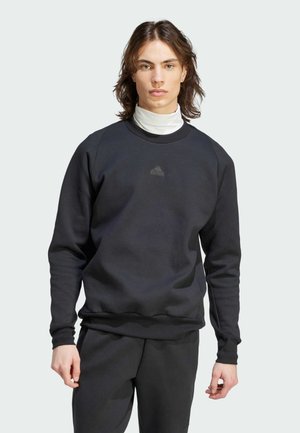 Czarna bluza z okrągłym dekoltem i prążkowanymi mankietami. Posiada małe, szare logo Adidas na piersi. Wydaje się być wykonana z miękkiego, teksturowanego materiału.