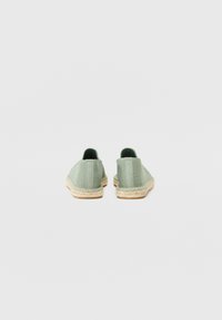 Groene mesh instapschoenen met een espadrille jute zool. De achterkant heeft verticale stiksels en gestructureerde accenten op de hak.