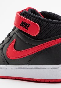 Svarta lädersneakers med röda accenter, inklusive Nike-logotypen och swoosh. Har en vadderad krage och vit strukturerad sula.