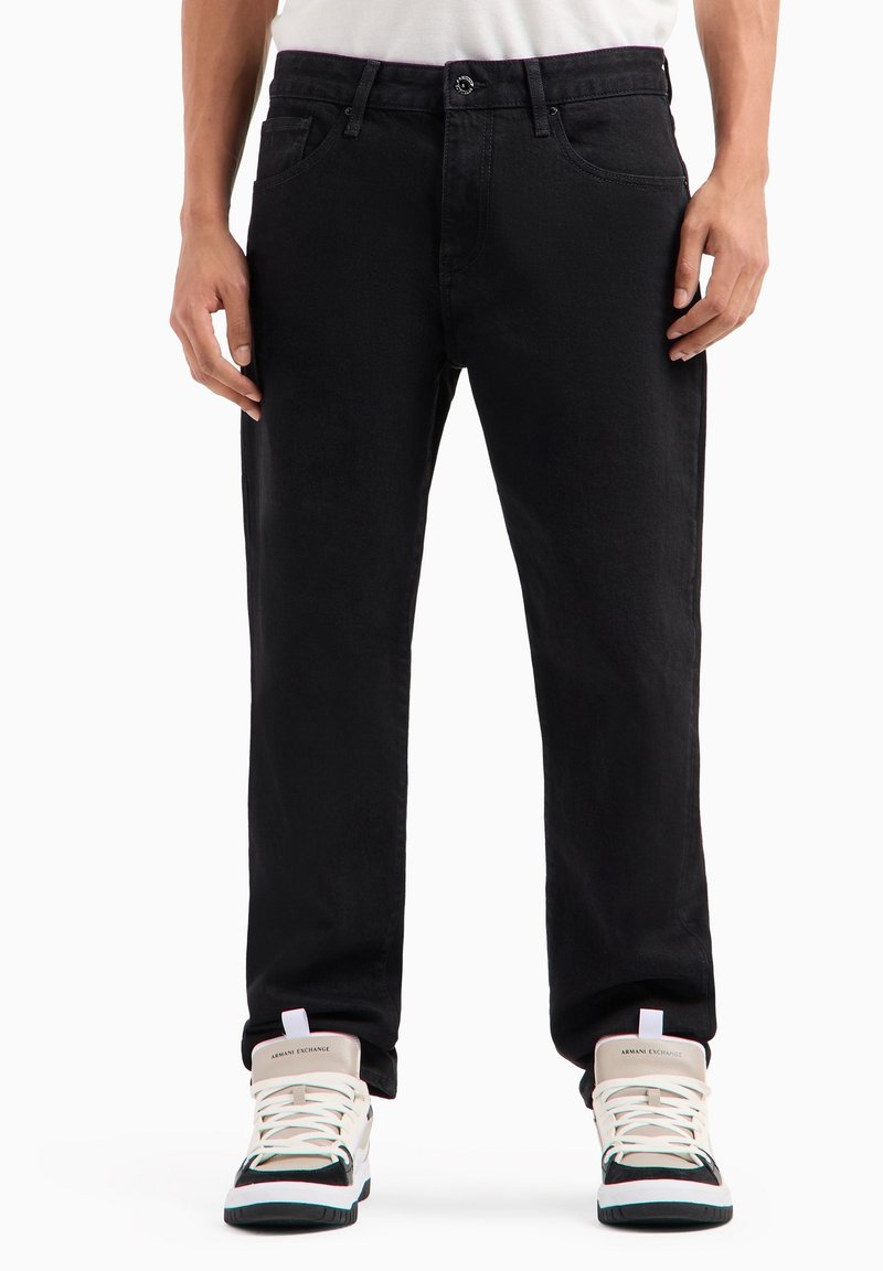 Jeans in denim nero caratterizzati da una vestibilità dritta e una chiusura a bottone. Abbinati a sneakers alte bianche con dettagli neri e teal.