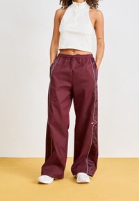 Burgundské sportovní kalhoty s bílými postranními pruhy, elastickým pasem a kapsami. V kombinaci s bílým halter topem a světlou obuví.