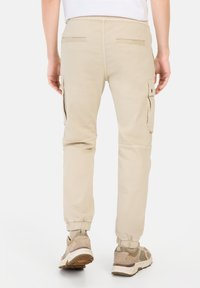 Beige Cargo-Hosen mit elastischen Bündchen, Nähte an den Hintertaschen und seitlichen Taschen. Weicher Stoff, stromlinienförmiges Design für Komfort und Funktionalität.
