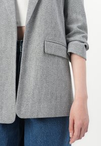 Grijze herringbone blazer met een notch-kraag, enkele zak en opgerolde mouwen; gecombineerd met high-waisted spijkerbroek.