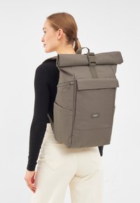 Zaino a roll-top in verde oliva tenue, realizzato in materiale resistente. Caratterizzato da un risvolto frontale, tasche laterali e spallacci regolabili per un maggiore comfort.