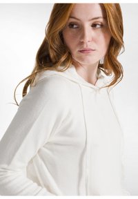 Sudadera blanca con capucha, hecha de una tela suave y con un corte relajado. Presenta una capucha con cordones y mangas largas con bordes acanalados.