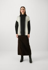 Maglione lavorato a maglia in bianco e nero con collo alto, caratterizzato da righe verticali, abbinato a una lunga gonna marrone e stivaletti neri.