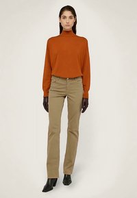 Suéter de cuello alto color óxido, pantalones ajustados color caqui, botines negros y guantes de cuero negros, presentados sobre un fondo neutro.