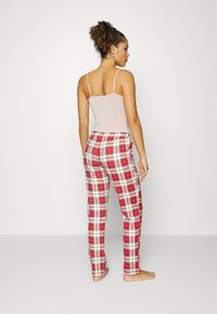 Lichtroze camisole gecombineerd met rode en witte geruite pyjamabroek. De broek heeft een trekkoord in de taille en zijzakken.