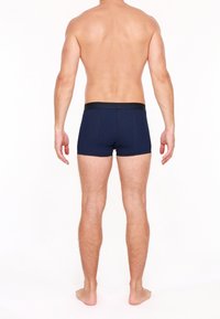 Des boxers bleu marine avec un motif de pois, dotés d'une ceinture élastique noire, présentés de dos sur un modèle masculin à la peau nue.