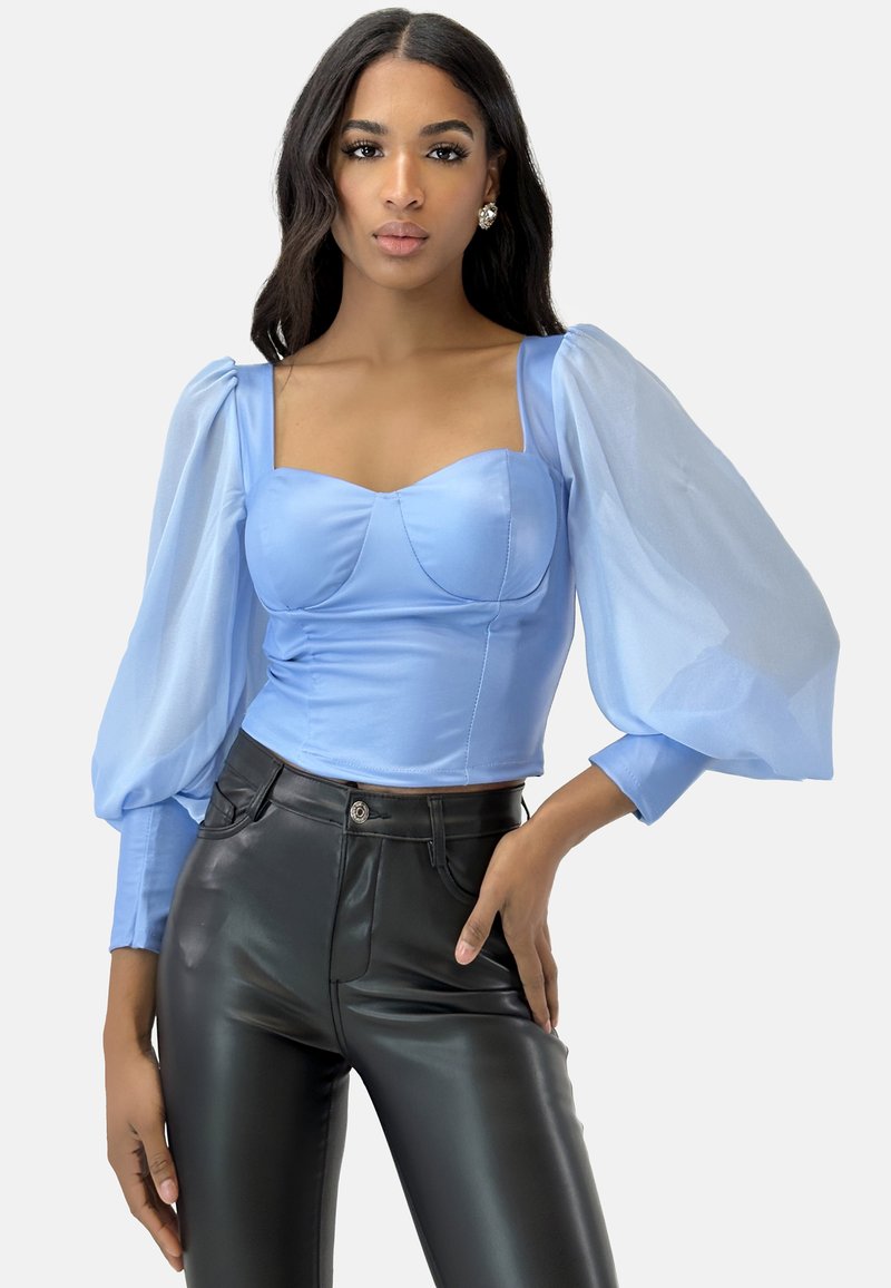 Lyseblå cropped top med struktureret skæring og gennemsigtige puffærmer, parret med sorte tætsiddende bukser. Glat stof, elegant design.