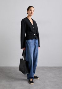 Black, textured blazer with a V-neck and front buttons, paired with wide-leg blue denim jeans and a black tote bag.
