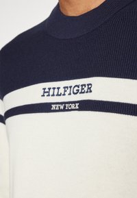 Maglione a maglia blu navy e bianco con righe orizzontali. "HILFIGER" e "NEW YORK" sono ricamati in blu navy sul petto.