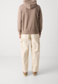 Huvtröja i brunt, med en avslappnad passform. Tillsammans med krämfärgade cargobyxor med sidofickor och smalnade ben. Bruna skor.