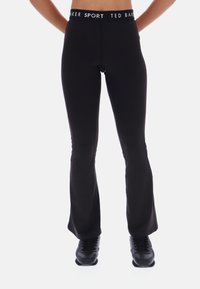 Čierne športové legíny s rozšíren�ým strihom a vysokým pásom, na ktorých sa nachádza biely pás s logom "Ted Baker SPORT", vyrobené z pružného a hladkého materiálu.