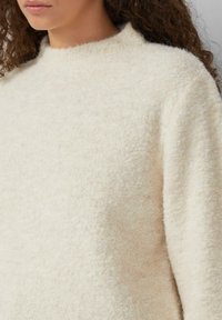 Kremowy, teksturowany sweter z wysokim kołnierzem; miękki, puszysty materiał; luźny krój; minimalne szwy i prosty design.