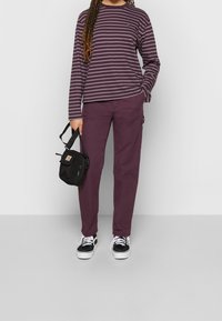 Long-sleeve purple striped shirt with crew neck, paired with solid purple pants. Black crossbody bag and black sneakers with white soles.