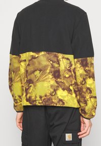 Felpa nera con un motivo marmorizzato giallo e marrone nella parte inferiore. Presenta una vestibilità comoda e polsini a costine.