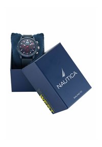 Montre Nautica dans une boîte marine, équipée d'un bracelet en silicone noir texturé, d'un cadran foncé avec des accents rouges et de quincaillerie argentée.