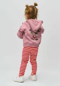 Rózsaszín kapucnis pulóver, amelynek hátulján grafikus cseresznye minta található, piros-fehér csíkos leggings-szel párosítva. Fehér tornacipő egészíti ki az öltözéket.