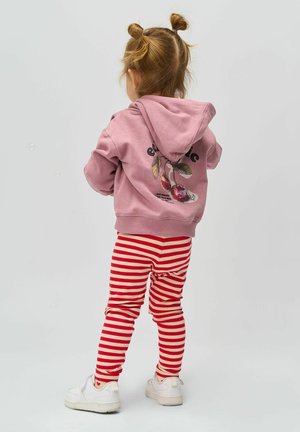 Sudadera rosa con un gráfico de cerezas en la parte posterior, combinada con leggins a rayas rojas y blancas. Zapatillas blancas completan el conjunto.