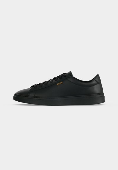 Baskets basses en cuir noir avec lacets noirs et logo subtil "BOSS" doré sur le côté, présentées sur un fond gris clair uni.
