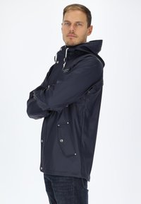Marineblauer wasserdichter Parka mit Kapuze, ausgestattet mit Druckknöpfen, seitlichen Taschen und elastischen Bündchen. Glatte, glänzende Textur mit lässiger Passform.