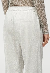 Joggers grigio chiaro con una sottile stampa leopardata, vita elastica e tasche laterali. Tessuto liscio e vestibilità comoda.