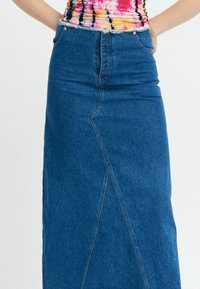 Sötétkék farmer szoknya, magasan ülő derékkal, két elülső zsebbel és ferde varrás részlettel elöl. Texturált anyag, közepes hosszúságú kialakítás.