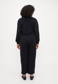 Black, textured top with long, sheer sleeves paired with high-waisted, wide-leg black pants. Styled with low-heeled black shoes.
